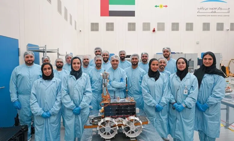 Team of scientists in clean suits posing with a Mars rover prototype.