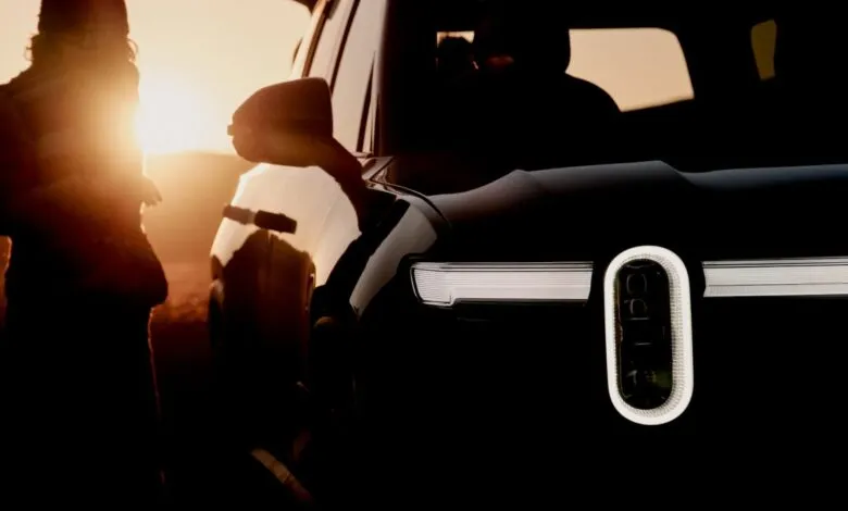 Silhouette of a person standing next to a black Rivian R1S electric SUV at sunset.