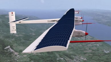 Solar Impulse 2 airplane with solar panels on its wings flying over a landscape.