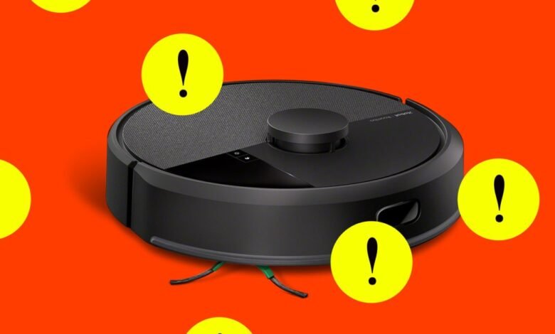 Black robot vacuum cleaner with yellow exclamation mark warning signs on an orange background.