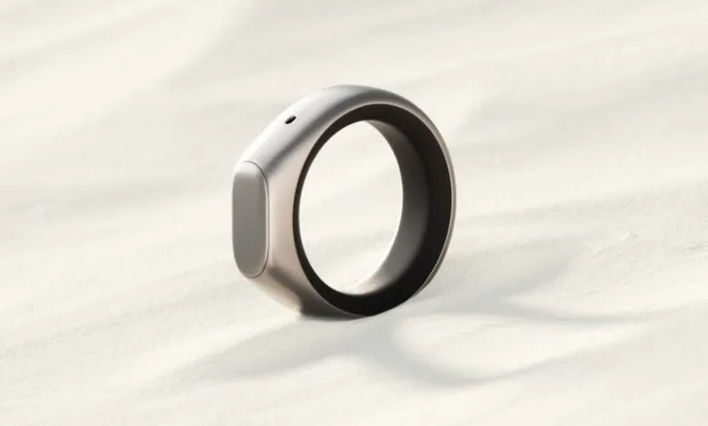 A sleek, silver smart ring with a dark interior rests on a textured, light-colored surface.