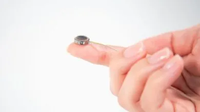 A person's finger holding a tiny medical implant with fine wires.