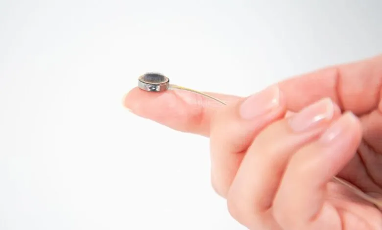 A person's finger holding a tiny medical implant with fine wires.