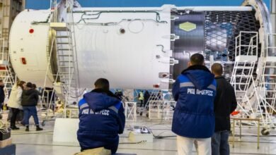Workers inspect a large white rocket stage with visible internal structure.