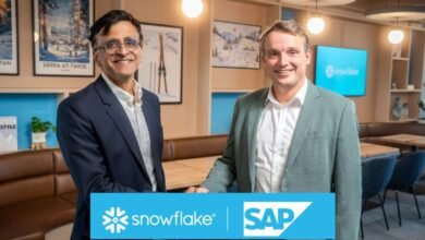 Two men in suits shaking hands in front of Snowflake and SAP logos.