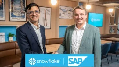 Two men in suits shaking hands in front of Snowflake and SAP logos.