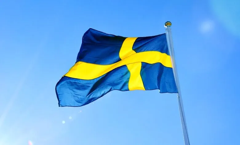 The Swedish flag with its blue background and yellow cross waves against a clear blue sky.