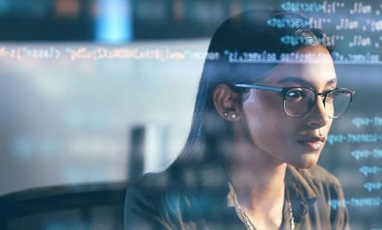 Woman with glasses looking at lines of code on a screen.