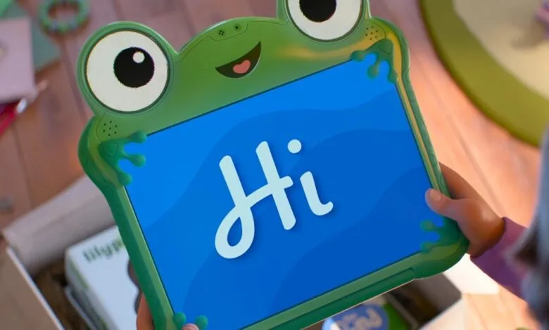 Child holding a green frog-shaped tablet displaying the word 'Hi' on a blue screen.
