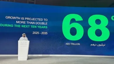 Man in traditional attire speaking at a podium with a large screen displaying economic growth projections.