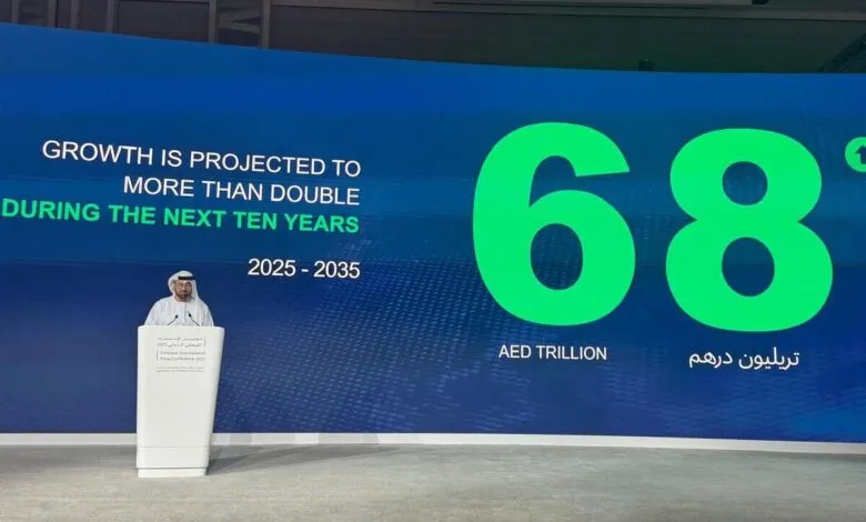 Man in traditional attire speaking at a podium with a large screen displaying economic growth projections.