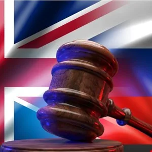 A wooden gavel rests on a sounding block against a blurred Union Jack flag.