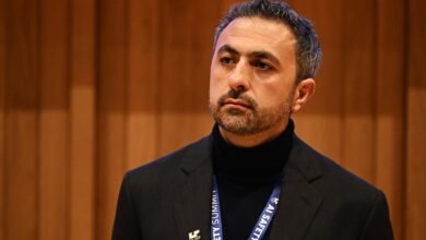 Man with beard and dark hair wearing a suit and turtleneck, looking to the side.
