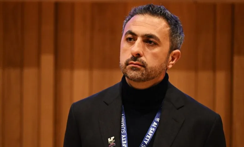 Man with beard and dark hair wearing a suit and turtleneck, looking to the side.