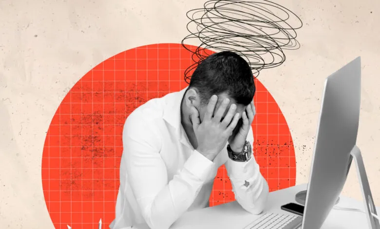 Man in white shirt with head in hands, looking stressed at a computer.