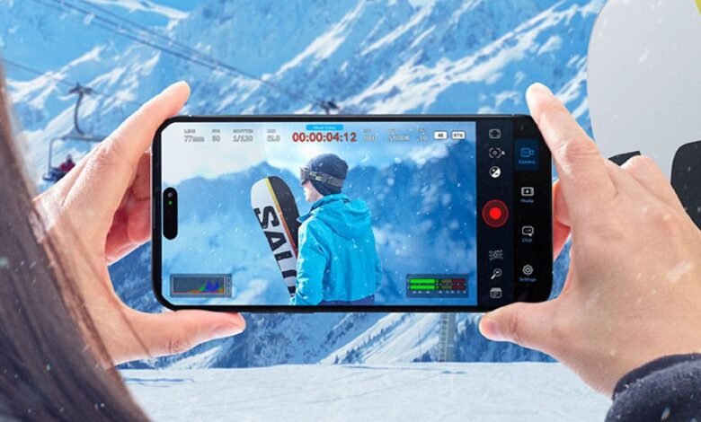 Person holding a smartphone recording a skier on a snowy mountain with a ski lift in the background.
