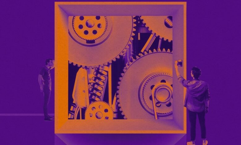 Two people observe a complex gear mechanism inside an open box.