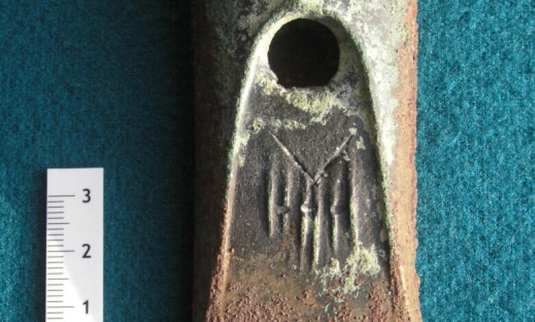 Close-up of an ancient bronze axe head with a circular hole and etched markings.