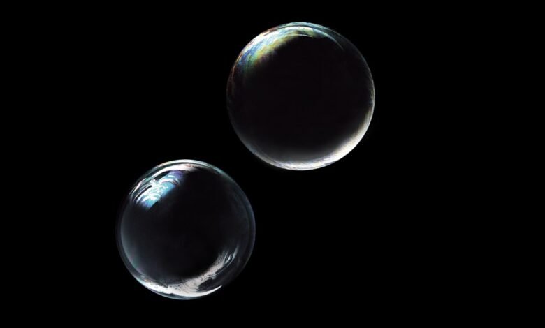 Two iridescent soap bubbles floating against a stark black background.