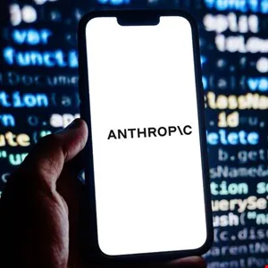 Hand holding a smartphone displaying the Anthropic logo against a backdrop of code.