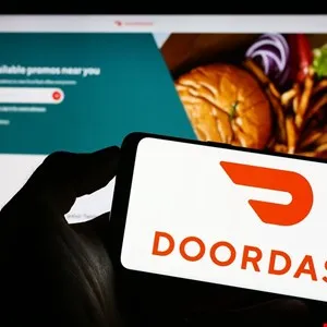 Hand holding a smartphone displaying the DoorDash logo and app interface.