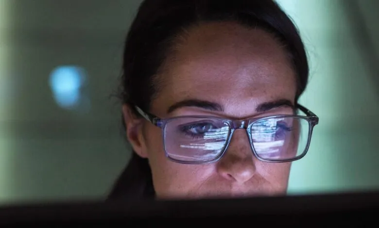 Close-up of a woman wearing glasses, with code reflected in the lenses.
