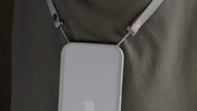 Close-up of a white iPhone with a crossbody strap attached, worn over a dark green shirt.
