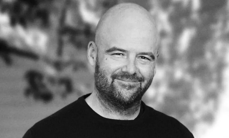 Black and white portrait of a smiling man with a beard and bald head.
