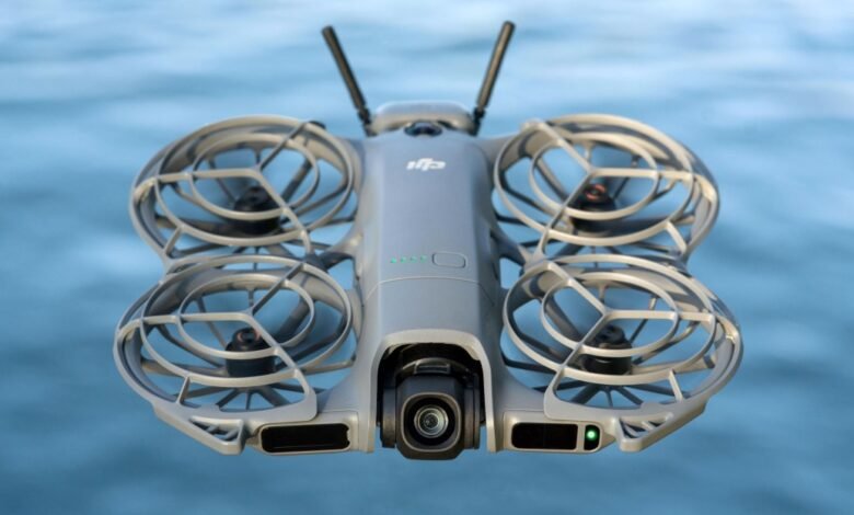 Close-up of a gray DJI drone with propeller guards hovering over blue water.