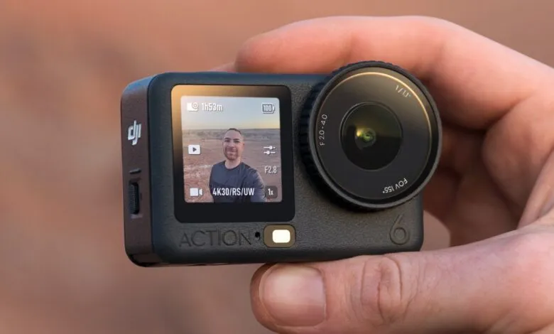 Close-up of a DJI Osmo Action 6 camera held in a hand, showing its screen and lens.