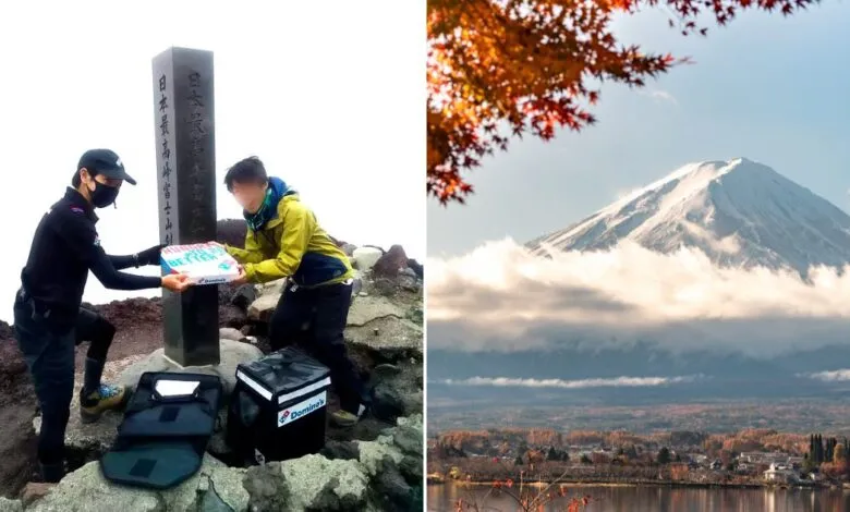 Two people in hiking gear with Domino's pizza boxes and delivery bags at the summit of Mount Fuji.