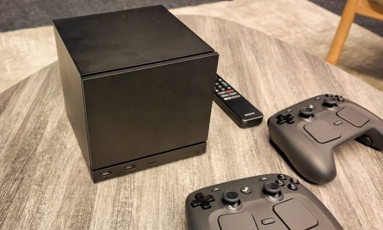 Black gaming console with two controllers and a remote on a wooden table.