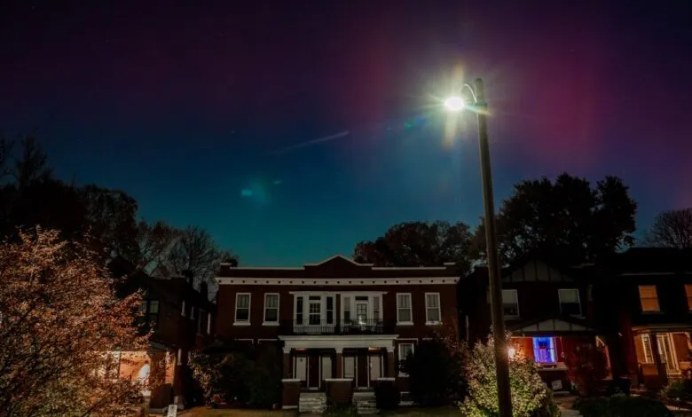 Streetlight illuminates a row of brick houses at night under a colorful sky.