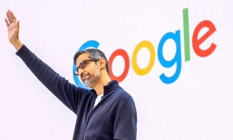 Sundar Pichai waves in front of the Google logo on a white background.