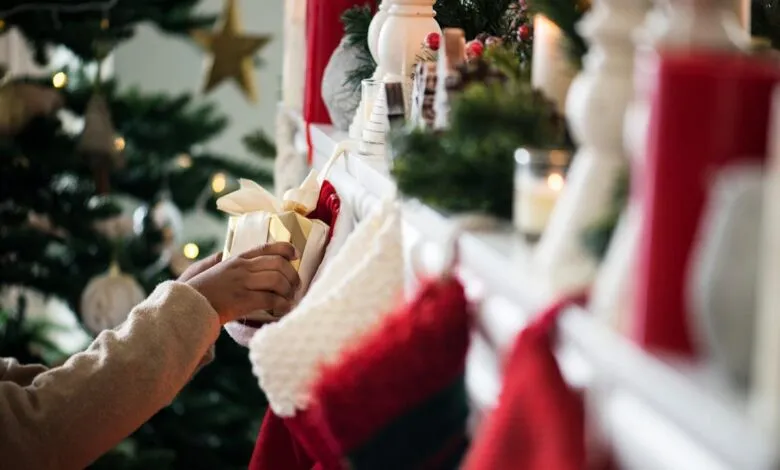 Hands placing a gold gift into a Christmas stocking on the mantel.