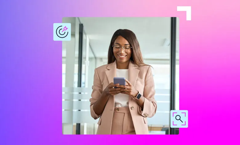 A smiling Black woman in a tan suit uses her smartphone in an office setting.