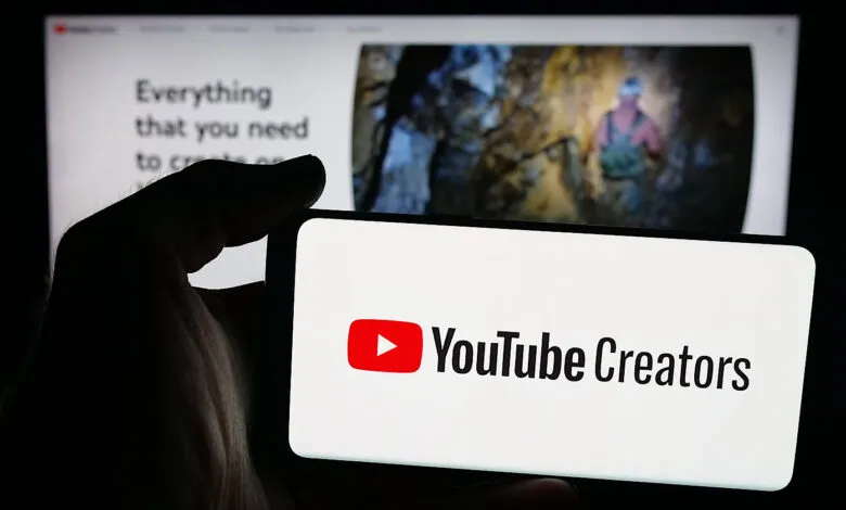 Hand holding a smartphone displaying the YouTube Creators logo and text.