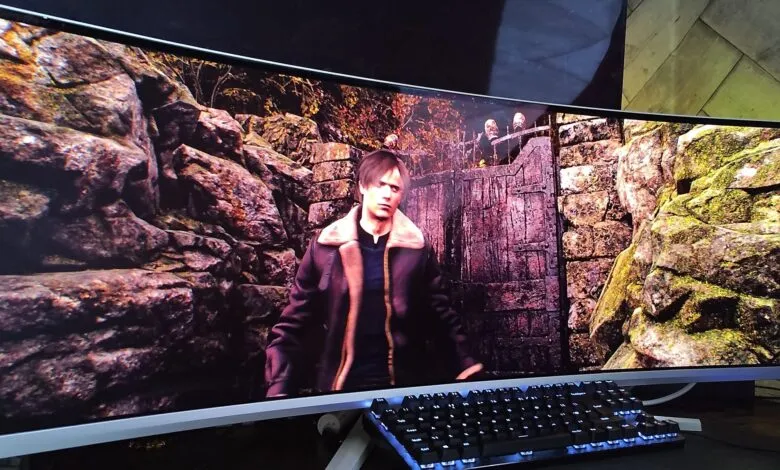 Leon S. Kennedy in a brown jacket stands before a wooden gate in a rocky, overgrown environment.