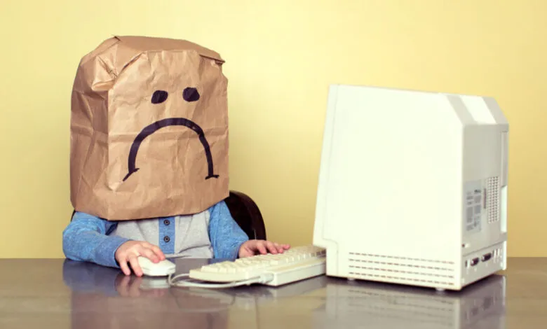 Child with a paper bag over their head, drawn with a sad face, using an old computer.