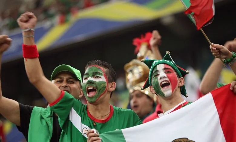 Excited soccer fans cheer, faces painted in Mexican flag colors.