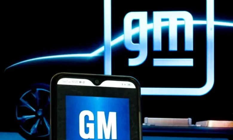 Smartphone displays the GM logo against a backdrop of a GM vehicle.