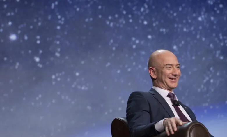 Jeff Bezos smiles while seated, with a starry blue background.