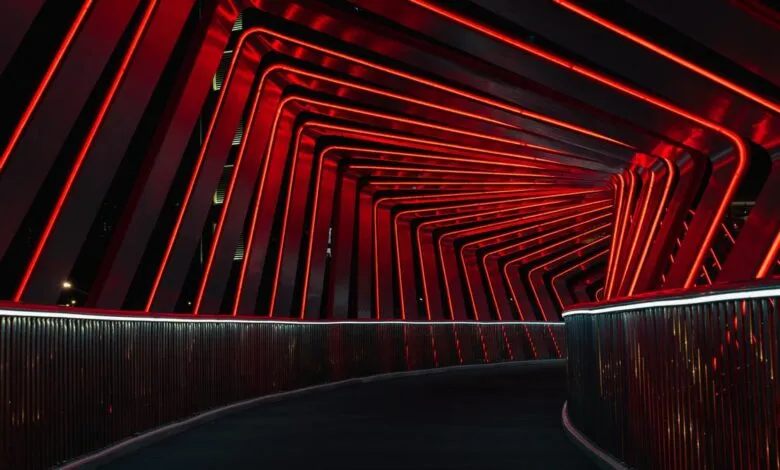 Red neon lights illuminate a curved pedestrian bridge at night.