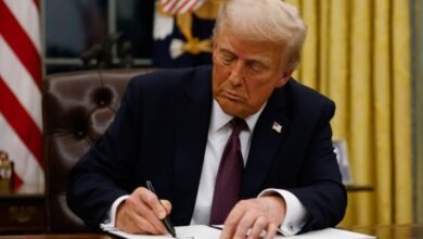 Donald Trump signing a document at the Resolute Desk in the Oval Office.