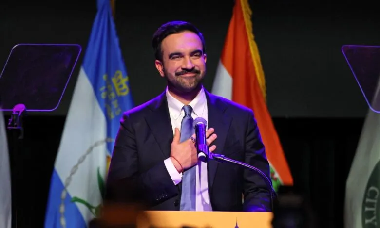 Man in suit with hand on chest speaking at podium with flags behind him.
