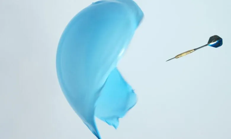 Dart pierces a blue water balloon against a white background.