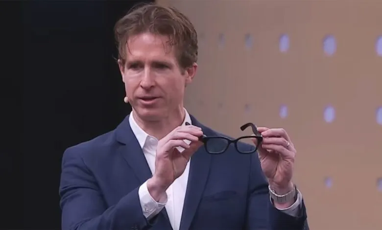 Man in a suit holding up a pair of black augmented reality glasses.
