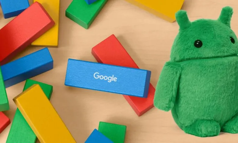 A green Android plush toy sits beside colorful Google-branded building blocks.