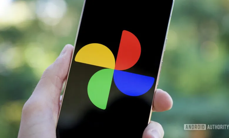 Close-up of a hand holding a smartphone displaying the Google Photos app logo.
