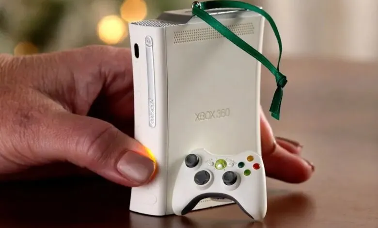 Close-up of a hand holding a white Xbox 360 console ornament with a green ribbon.